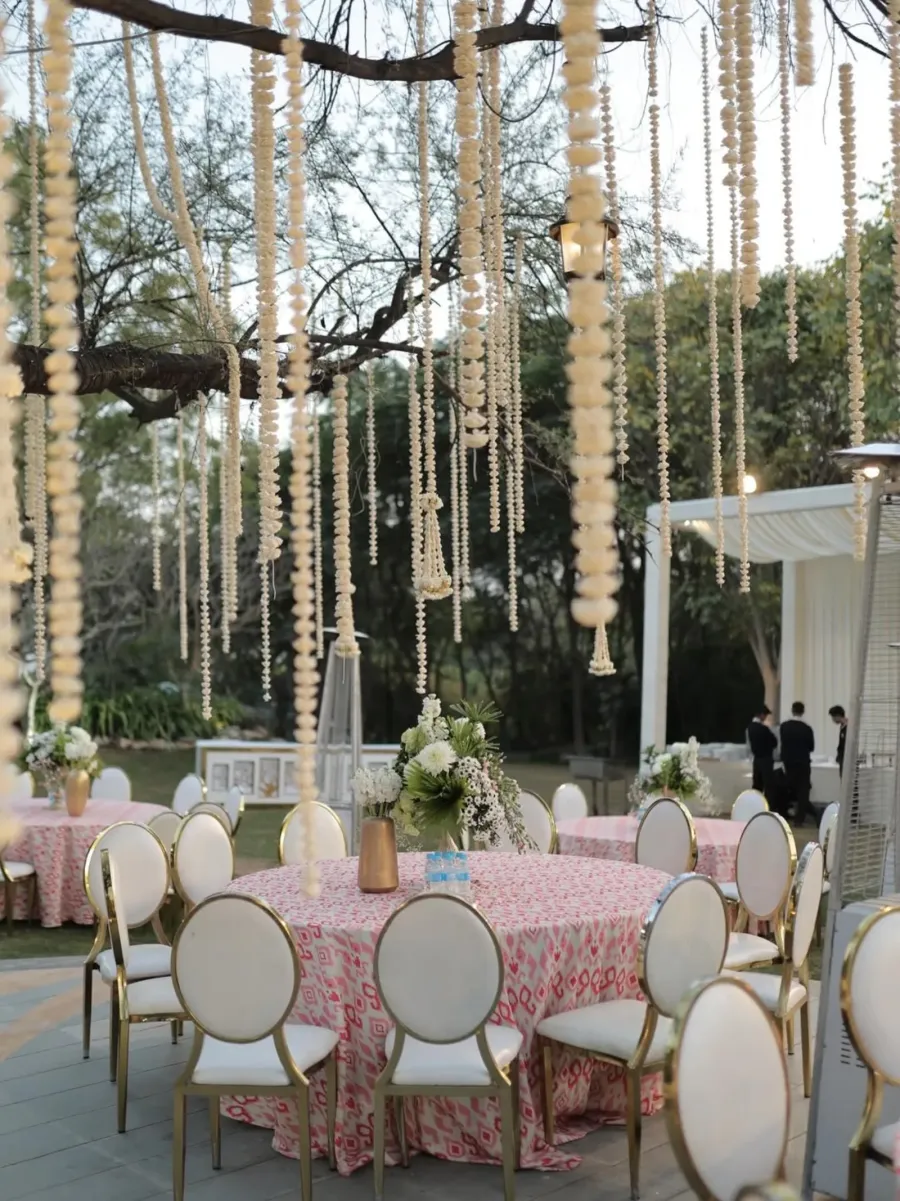 Floral strands hanging over round dining tables beneath the trees