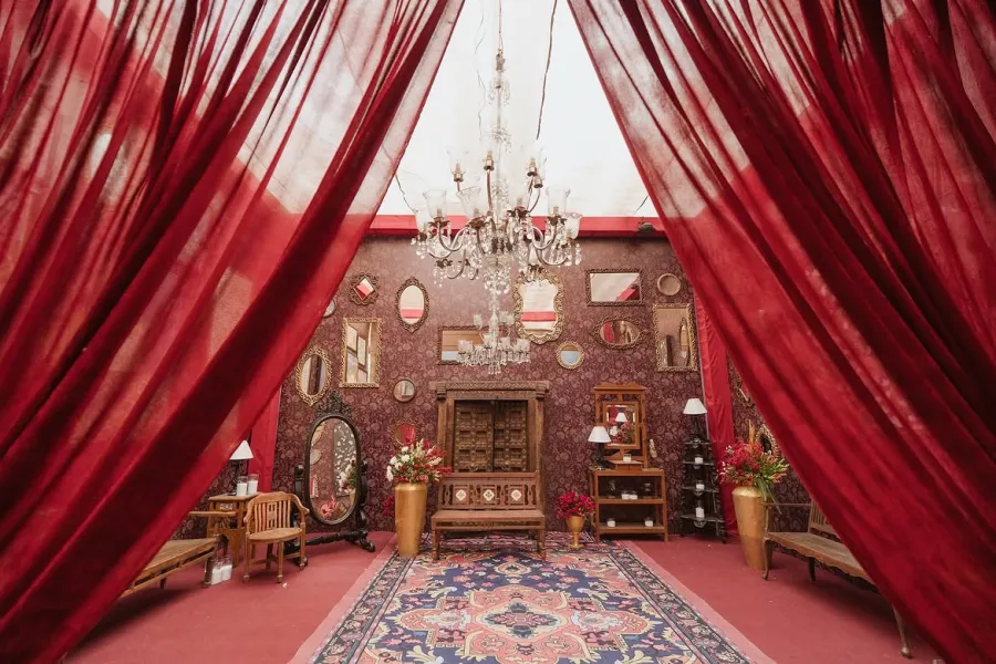 Deep red draped corner with a chandelier, patterned carpet and antique furniture